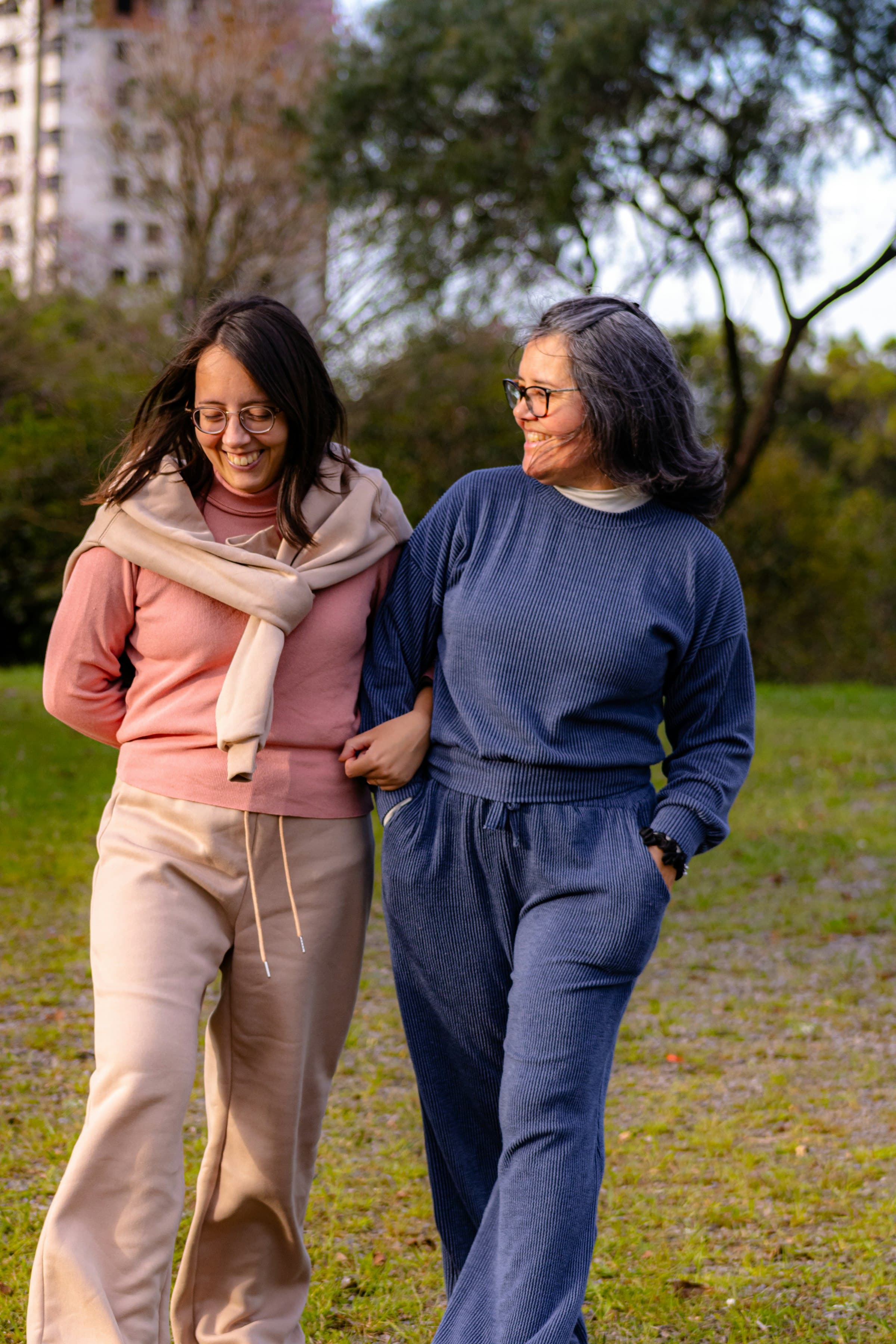 Two women walking arm in arm through a park, smiling and talking