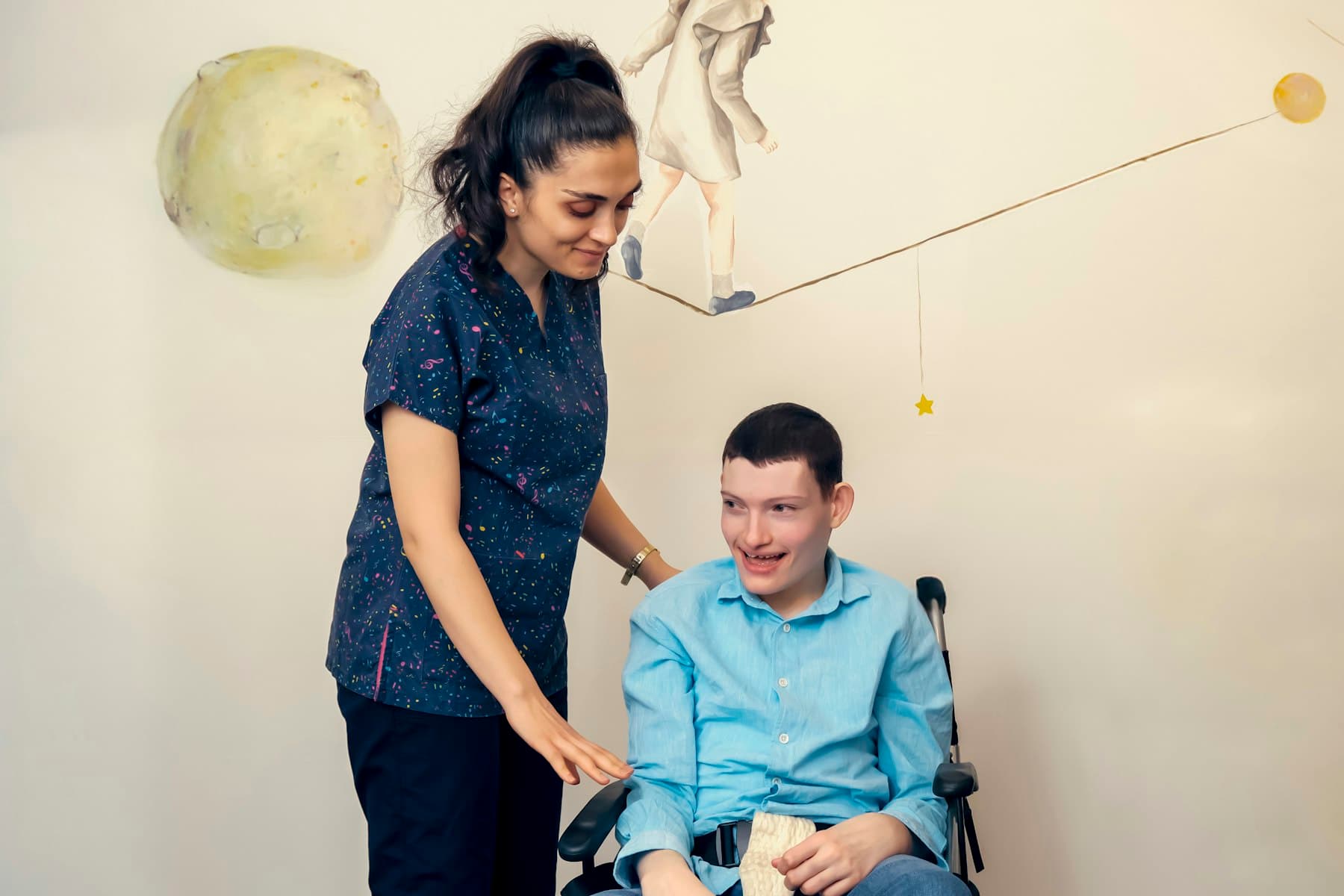 A support professional smiling with a young man who uses a wheelchair